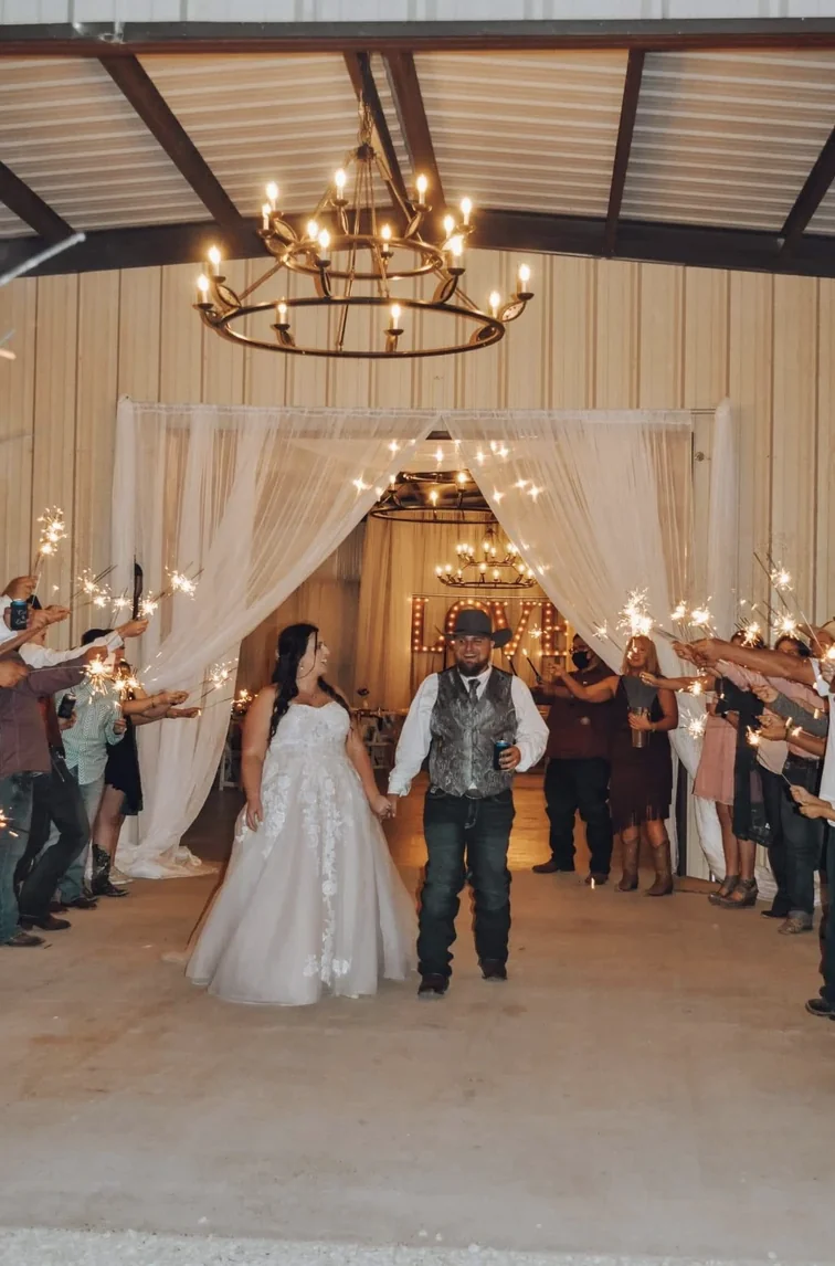 Guests celebrating as Cole and Emily exit through the draped barn doorway beneath a LOVE marquee sign