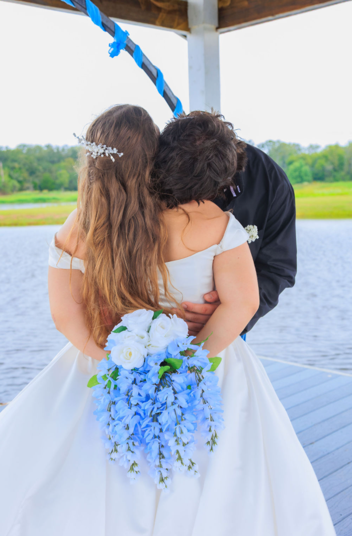 Jaelyn & Keelan's wedding at Reverie at Diamond D — the bride and groom embracing on the dock with the blue-and-white bouquet in the foreground
