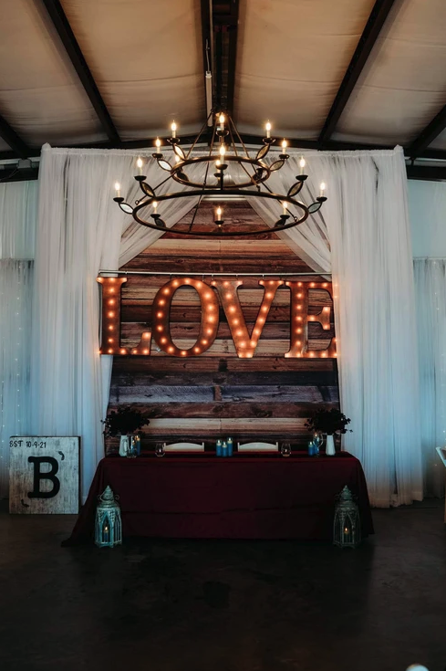 Sweetheart table beneath the iron chandelier and glowing LOVE marquee on the reclaimed wood wall