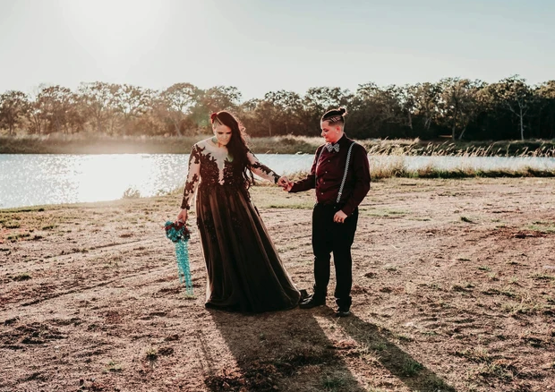 Couple walking hand in hand by the lake in warm sun flare with a teal bouquet