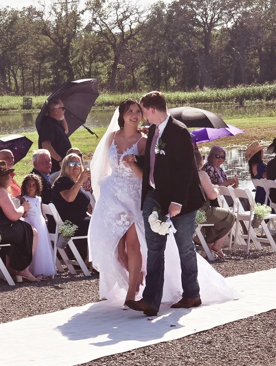 Newlyweds smiling as they walk back up the aisle past cheering guests beside the lake