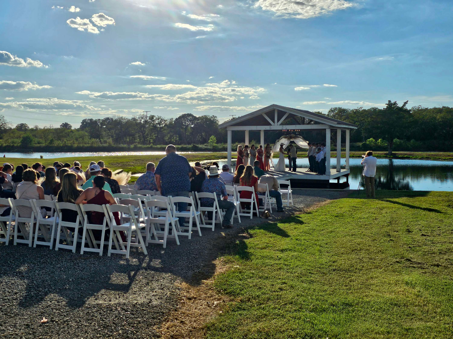 Guests seated in white chairs during an outdoor wedding ceremony beside the lake