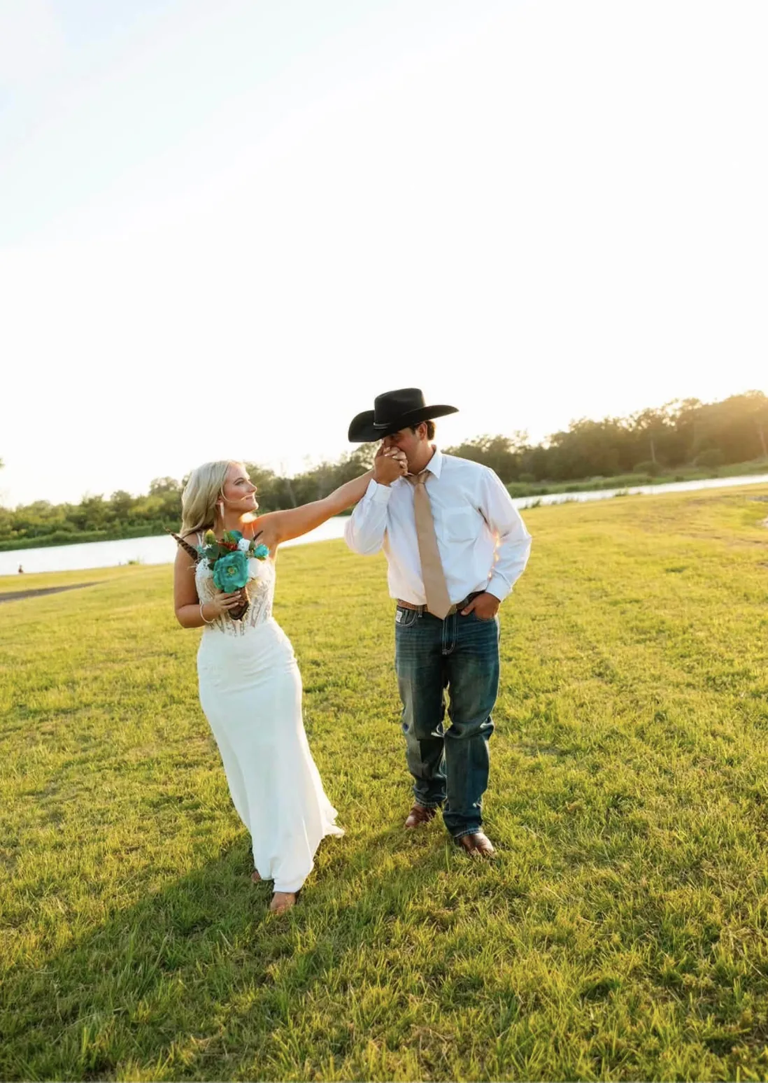 Bride and groom kissing hands at golden hour on the lakeside lawn at Reverie at Diamond D near College Station, Texas