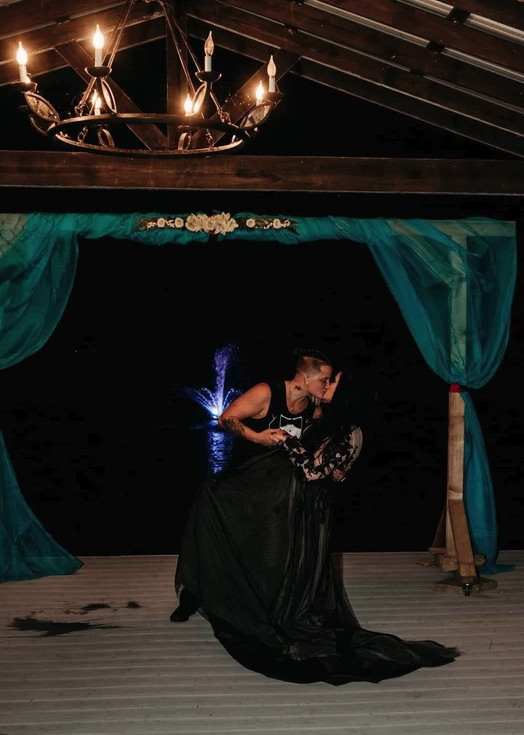 Couple sharing a dramatic first dance dip under the wrought-iron chandelier and teal draping