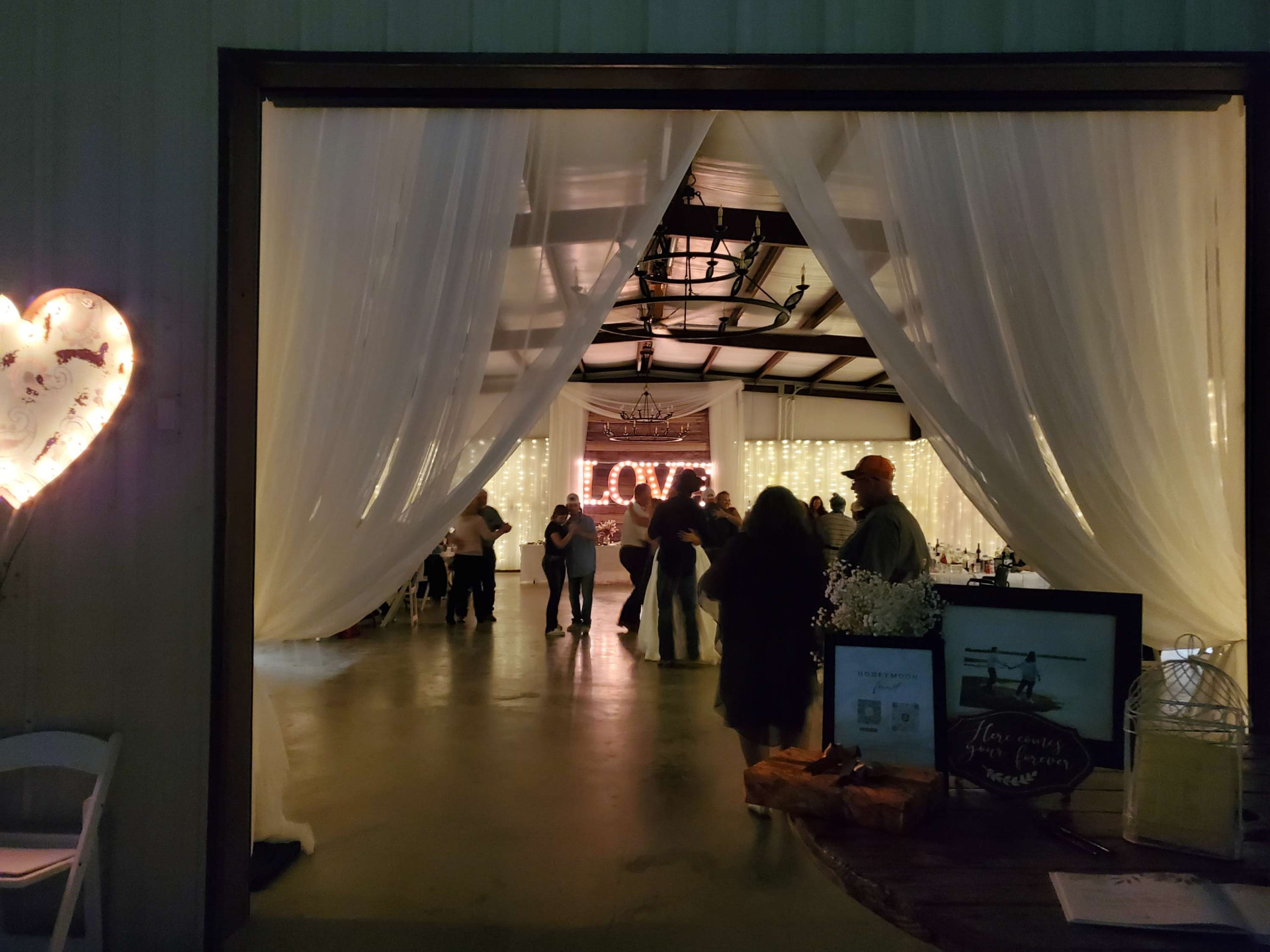 Guests dancing under string lights and chandeliers in the barn during a wedding reception