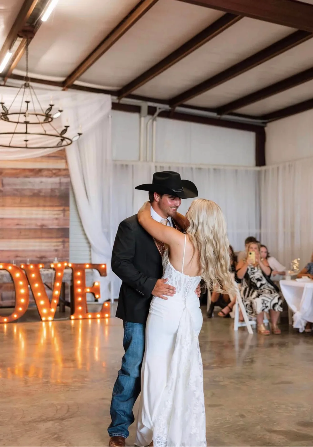 First dance beneath the iron chandelier and LOVE marquee letters inside the barn at Reverie at Diamond D