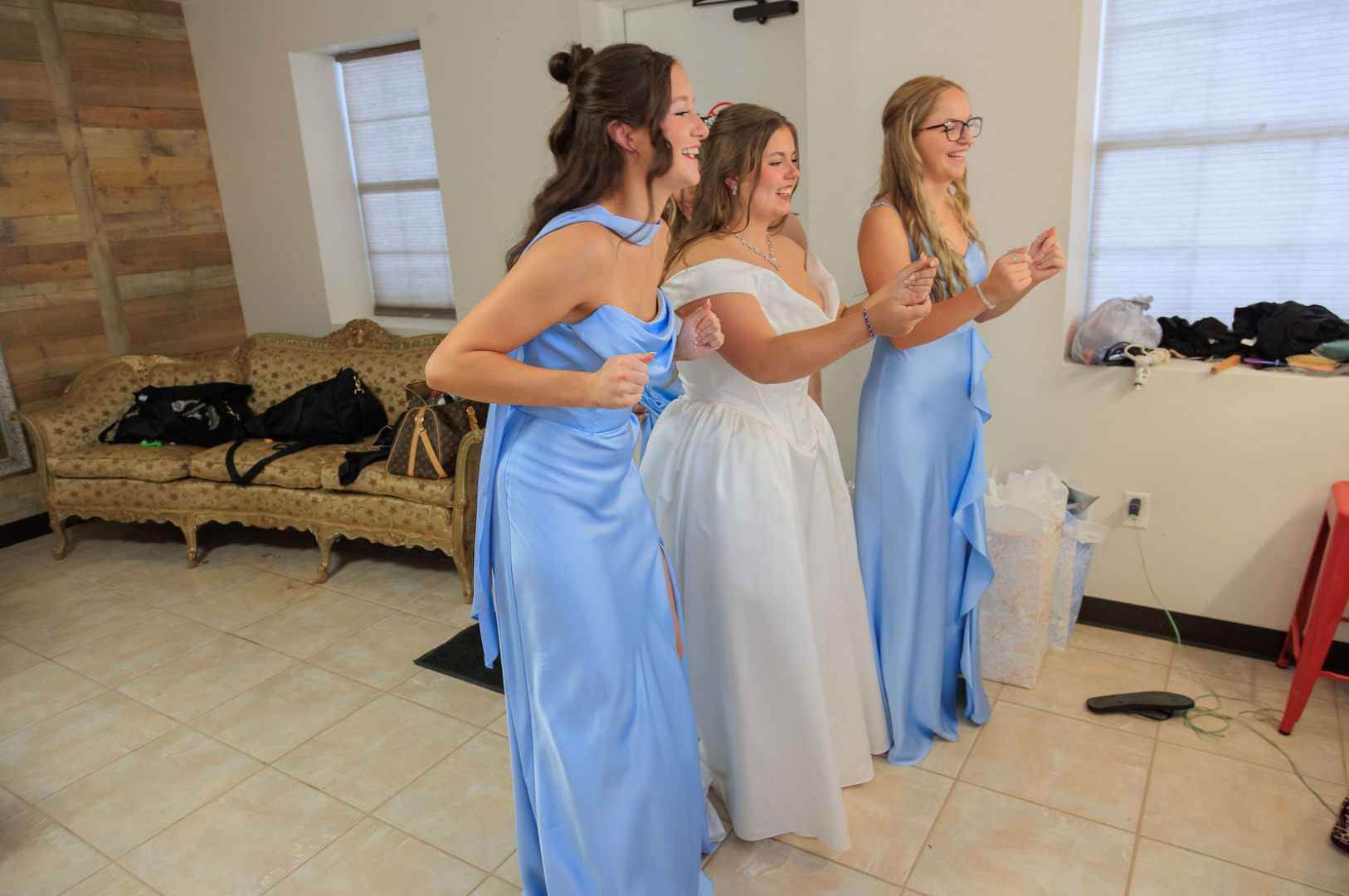 Jaelyn & Keelan's wedding at Reverie at Diamond D — the bride laughing with her bridesmaids in light blue gowns in the bridal suite