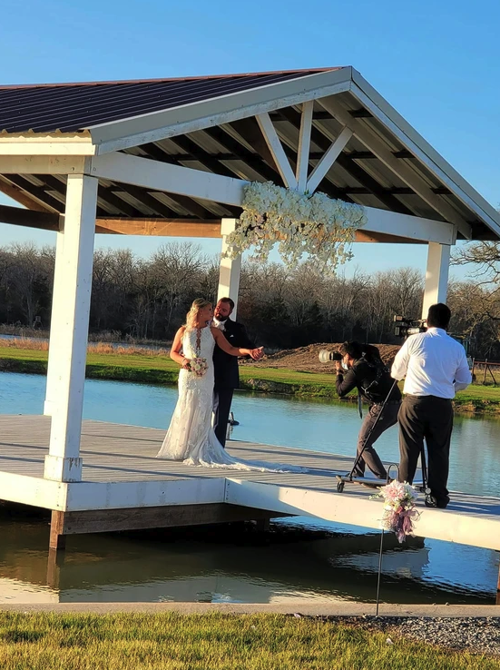 Newlyweds photographed on the lakeside pavilion under a white floral installation