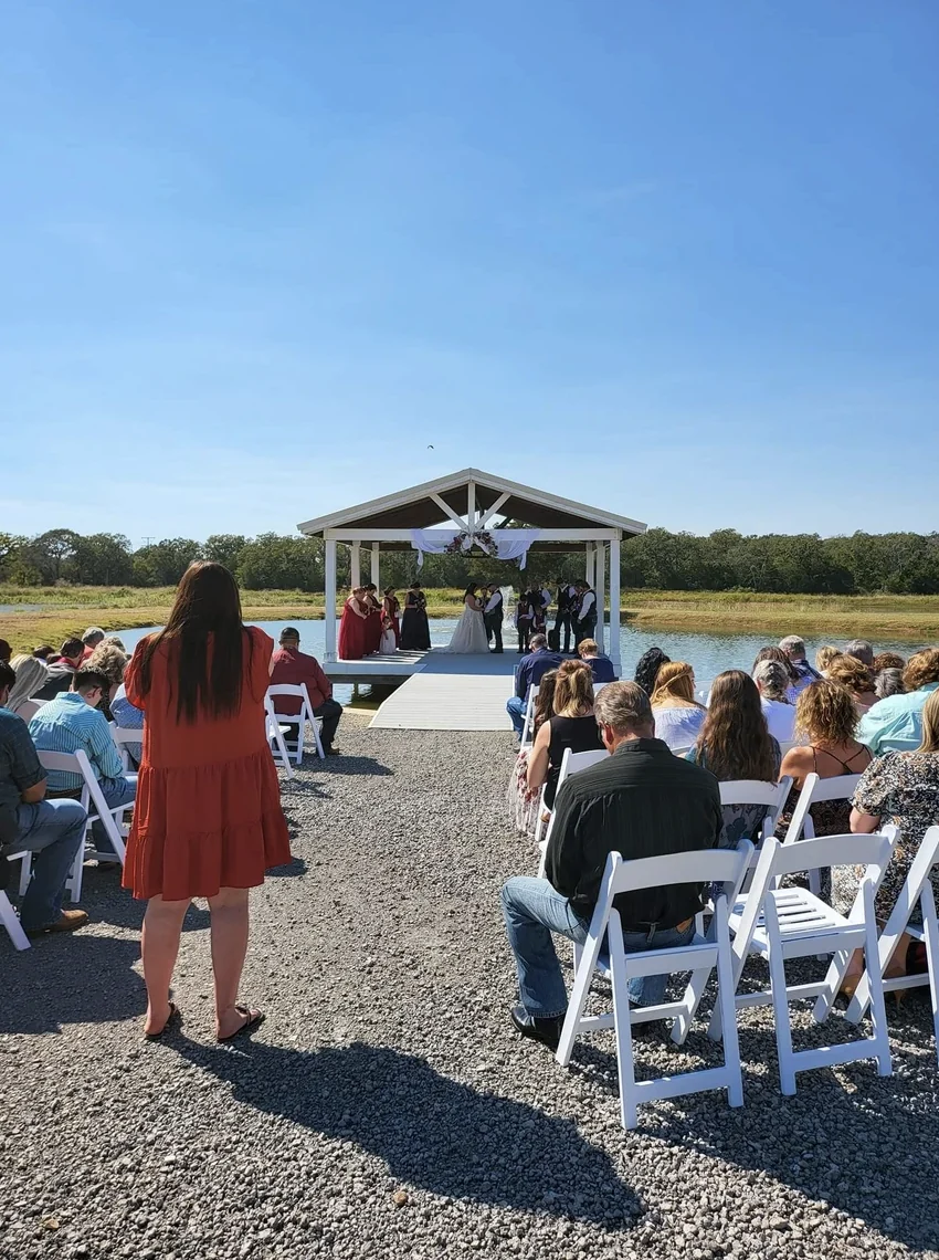 View up the aisle toward the lakeside pavilion with guests seated on both sides at an outdoor Texas wedding