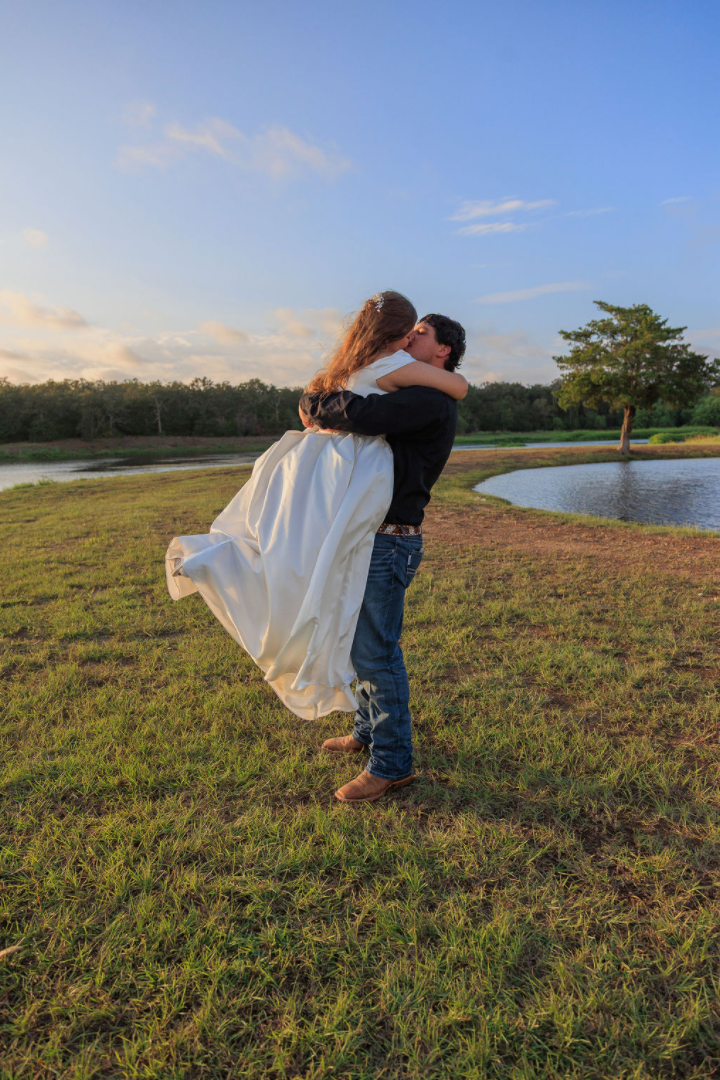 Jaelyn & Keelan's wedding at Reverie at Diamond D — the groom holding the bride as they kiss by the lake at golden hour