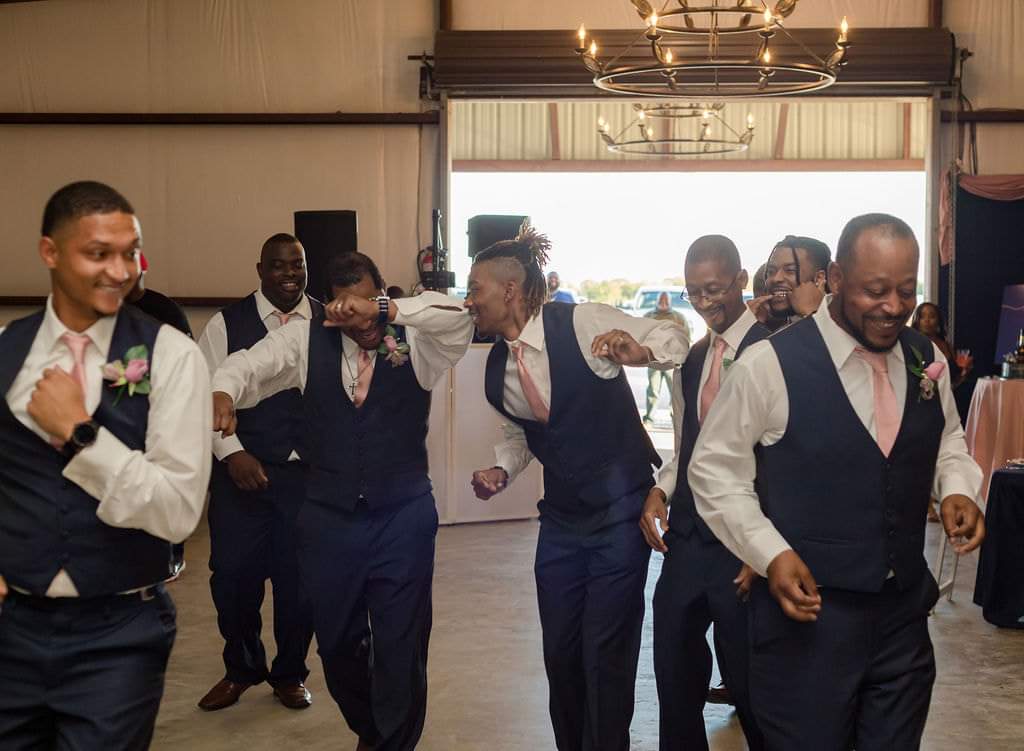 Groomsmen in navy vests dancing into the barn reception