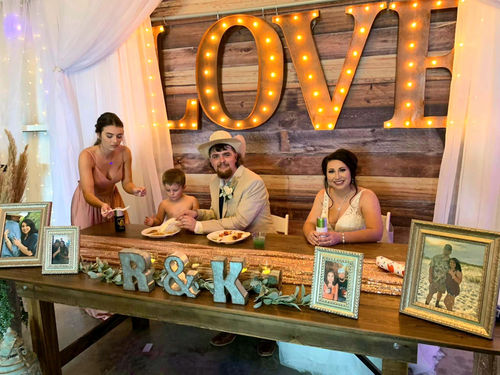 Sweetheart table with monogram letters and family photos under a marquee LOVE sign