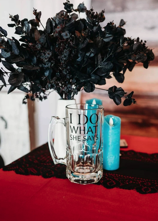 Black eucalyptus centerpiece with a teal candle and etched glass mug on red and black lace linens
