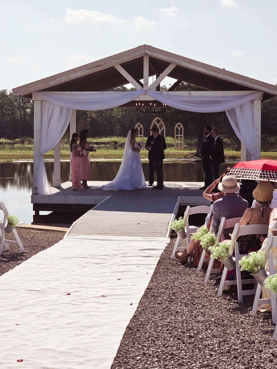 Bride and groom exchanging vows on the lakeside pavilion while guests watch from the aisle at Reverie at Diamond D