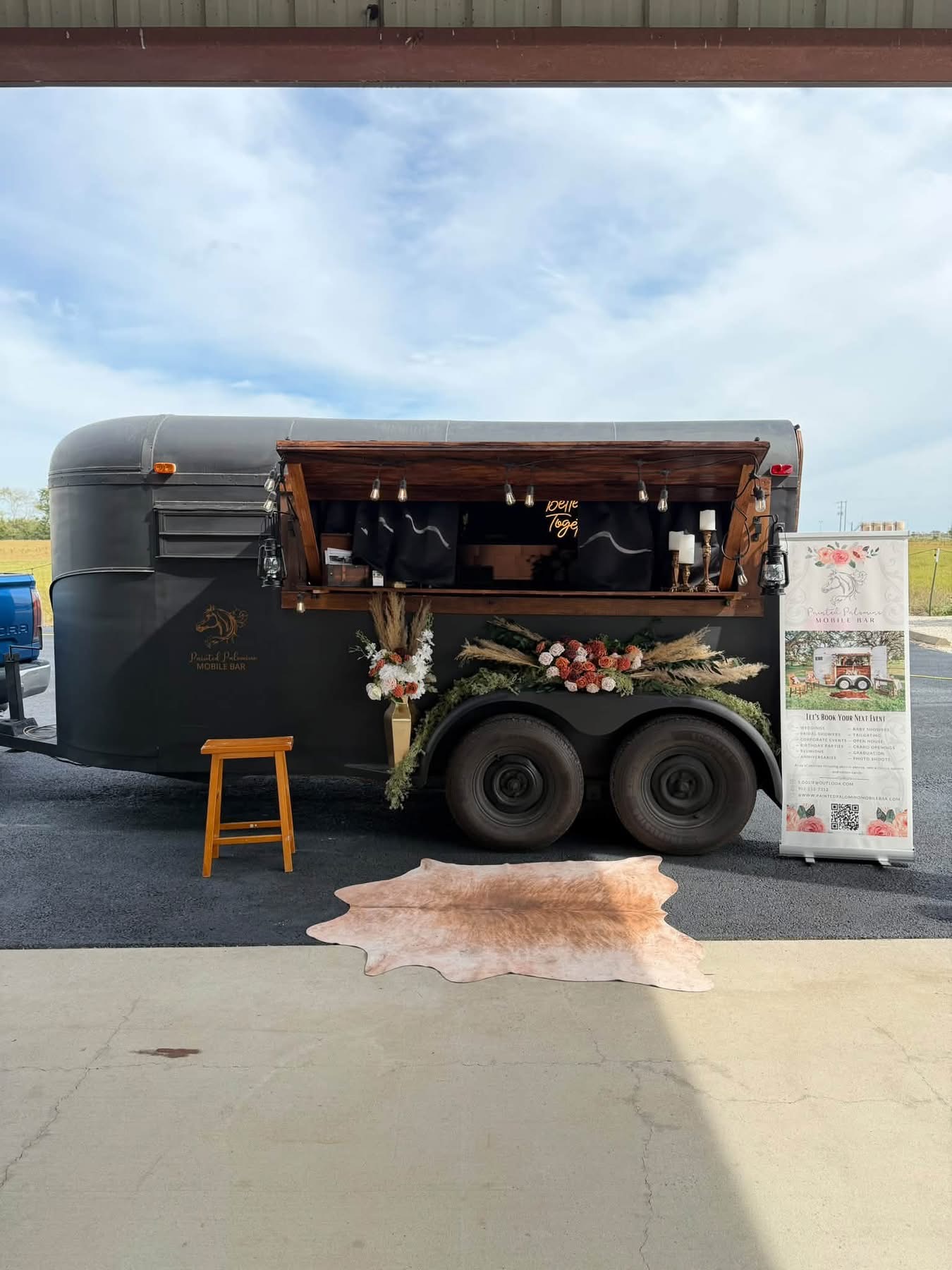 October 2026 Open House at Reverie at Diamond D wedding venue in Normangee, Texas — a mobile bar trailer styled with florals and a cowhide rug outside the barn