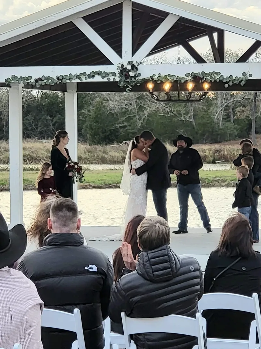 Bride and groom share their first kiss at the lakeside pavilion gazebo at Reverie at Diamond D wedding venue in Texas