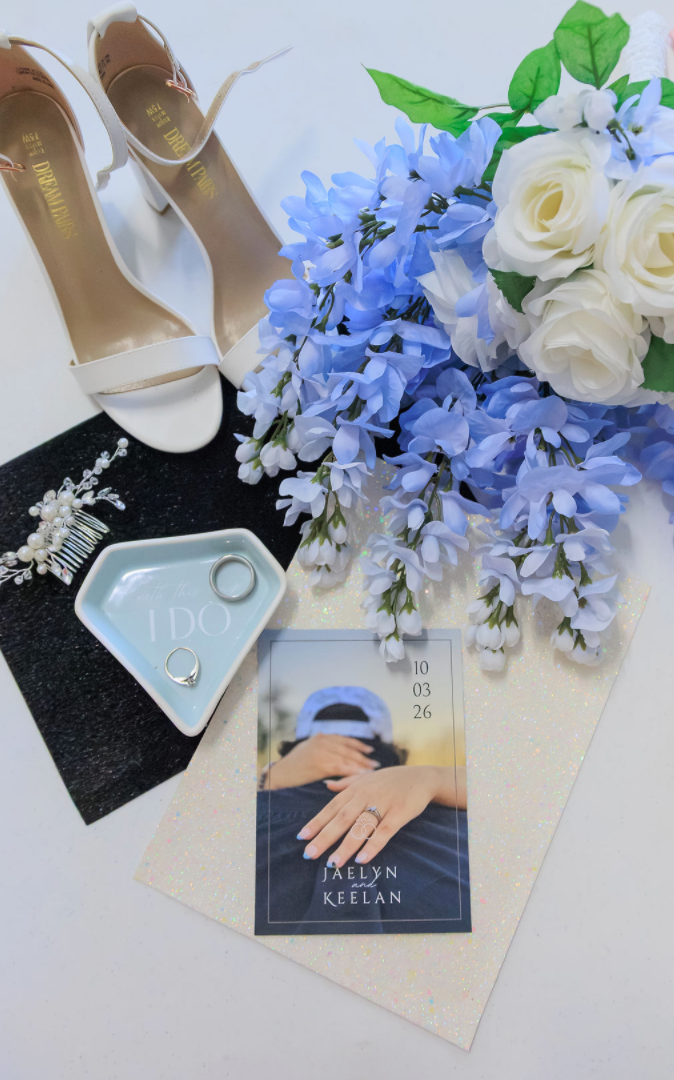 Jaelyn & Keelan's wedding at Reverie at Diamond D — flat-lay of white heels, the blue bouquet, ring dish, and the couple's invitation