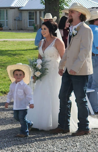 Bride and groom in cowboy hats walking with their ring bearer after the ceremony