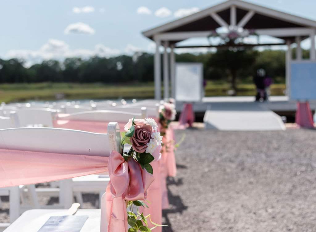 Blush rose aisle markers leading toward the white lakeside ceremony pavilion