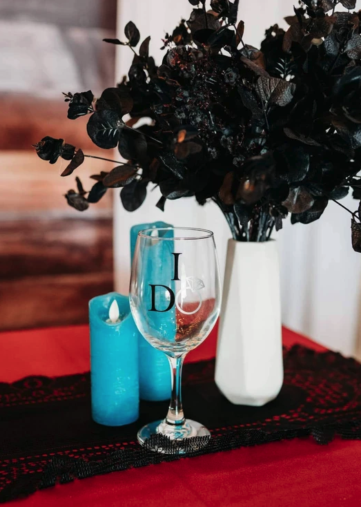 I Do wine glass with a teal candle and black eucalyptus arrangement on red and black lace linens