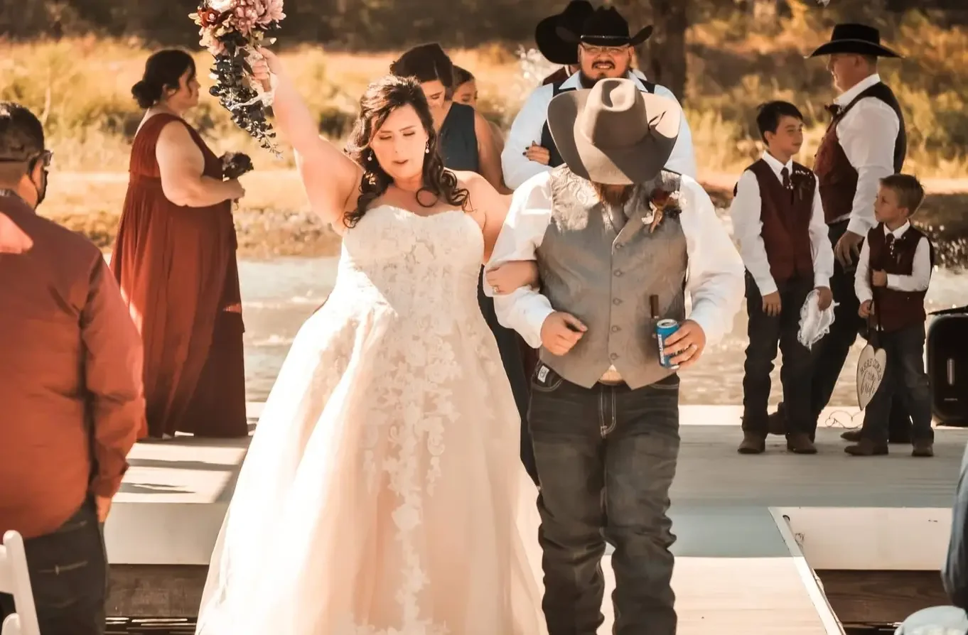 Bride raising her bouquet in celebration as she walks back up the aisle arm in arm with the groom at a Texas wedding