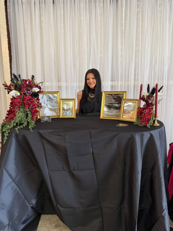 October 2026 Open House at Reverie at Diamond D wedding venue in Normangee, Texas — a vendor booth styled with burgundy florals and gold-framed wedding portraits