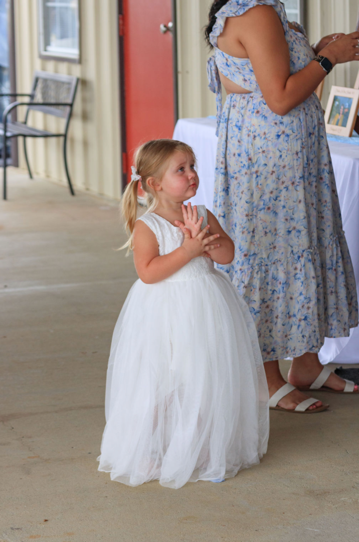 Jaelyn & Keelan's wedding at Reverie at Diamond D — a flower girl in a white tulle dress standing with a guest