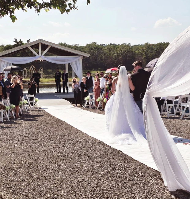 Bride's processional down the linen aisle runner toward the lakeside pavilion at Reverie at Diamond D