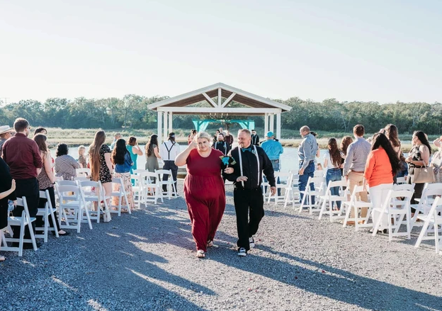 Guests celebrating the recessional down the white chair aisle from the lakeside pavilion