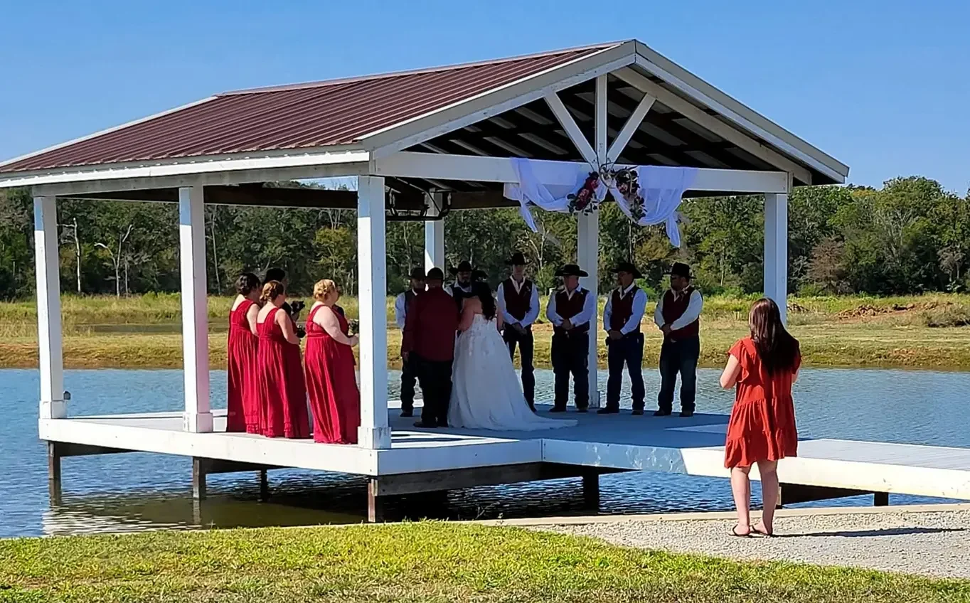 Wedding party in red gathered on the lakeside dock pavilion as Cole and Emily exchange vows over the water