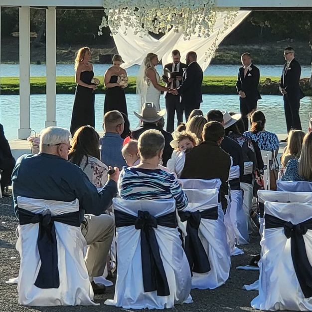 Couple exchanging vows beneath a floral chandelier as guests look on