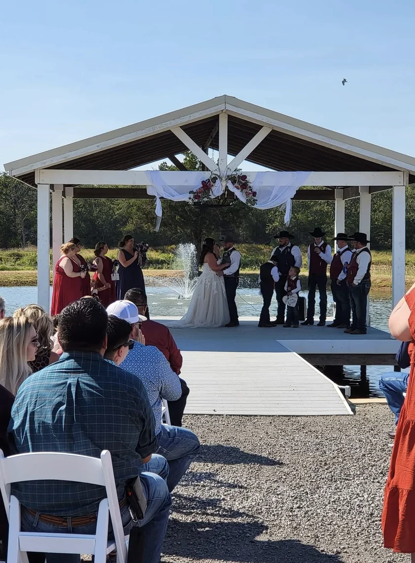 Guests seated on white folding chairs watching Cole and Emily's wedding ceremony at a Texas country wedding venue