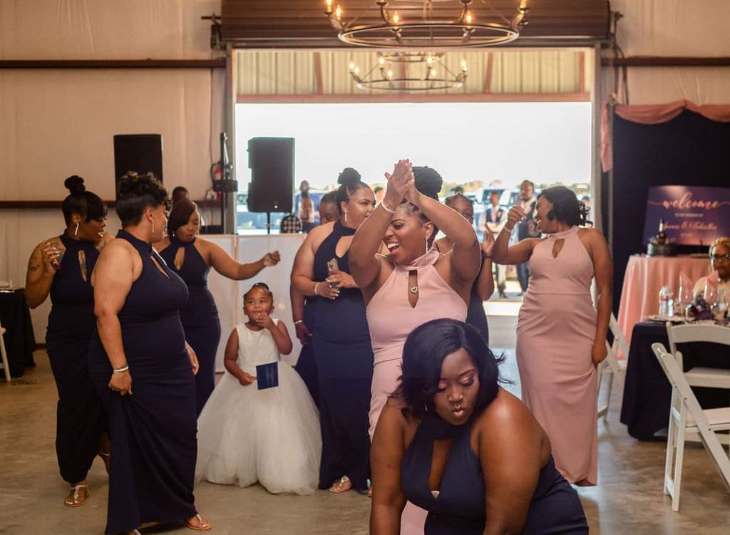 Bridesmaids in navy and blush gowns dancing on the barn floor