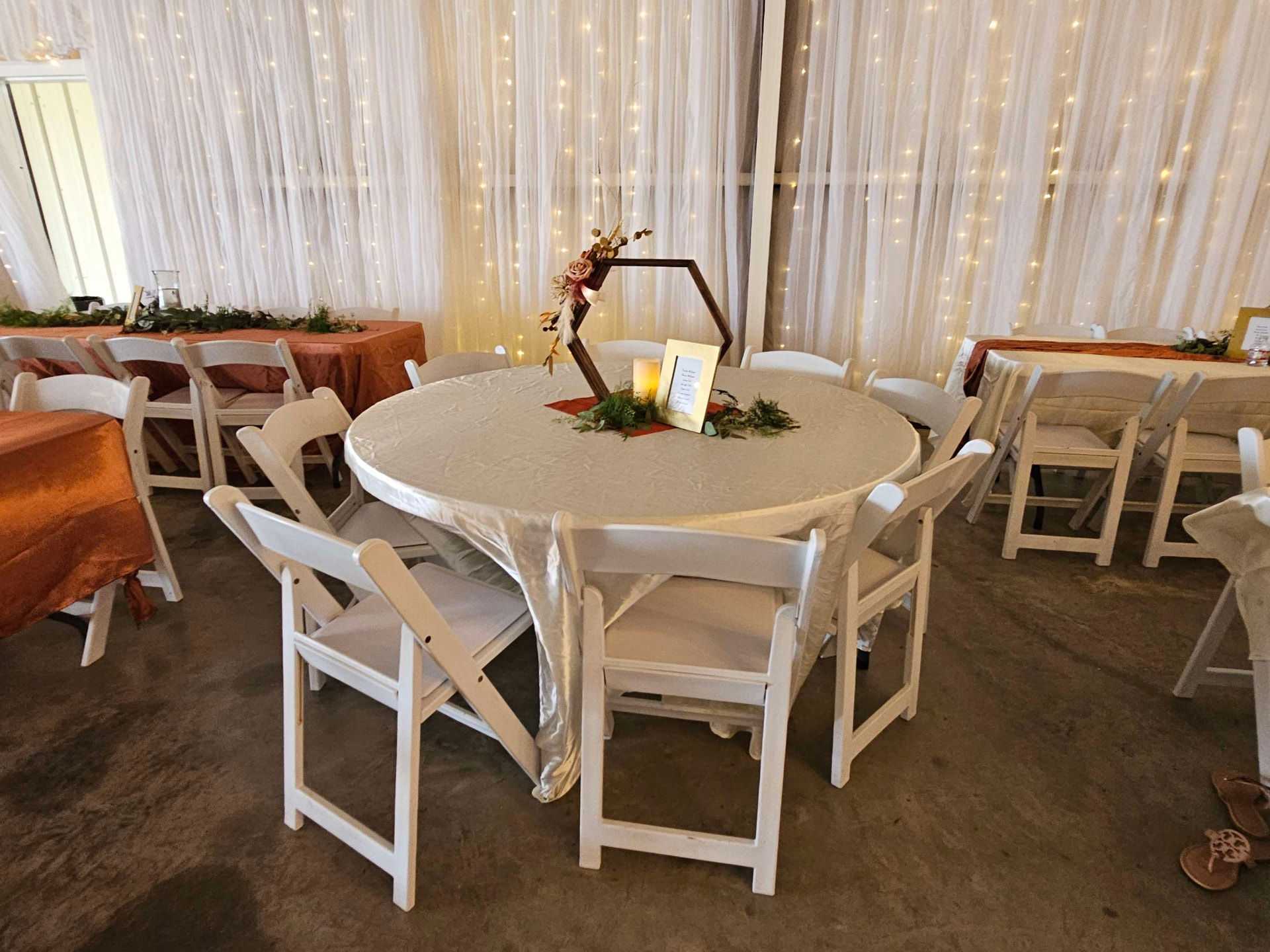 Round guest table with hexagon centerpiece in front of string-light draping at Reverie at Diamond D