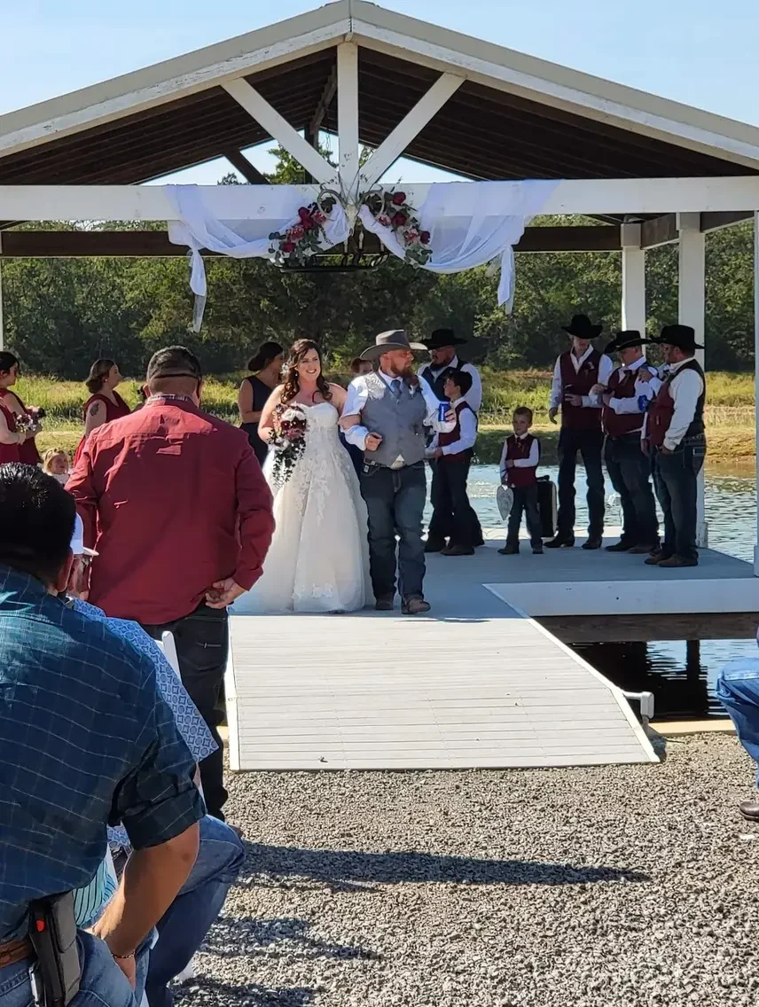 Bride escorted down the aisle toward the lakeside pavilion as guests turn to watch