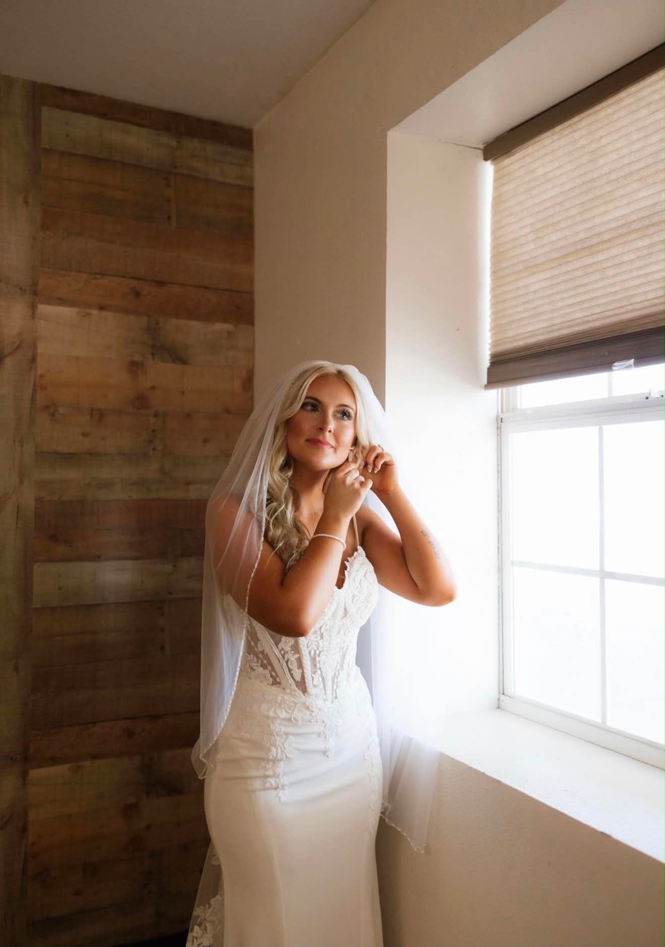 Bride getting ready by the window against the reclaimed wood wall of the bridal suite at Reverie at Diamond D