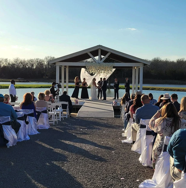 Wide view of the lakeside pavilion ceremony with the wedding party on the dock