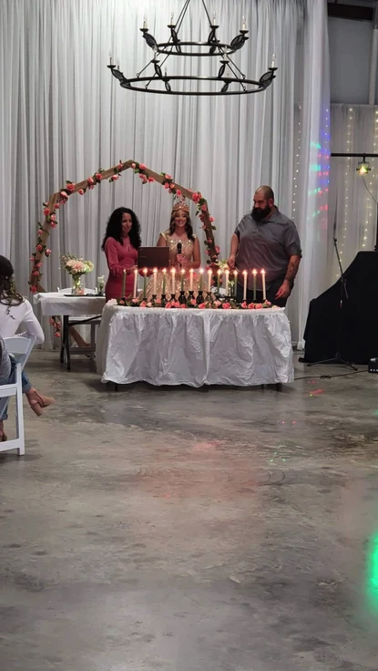 Sixteen lit candles on the ceremony table framed by the coral floral arch