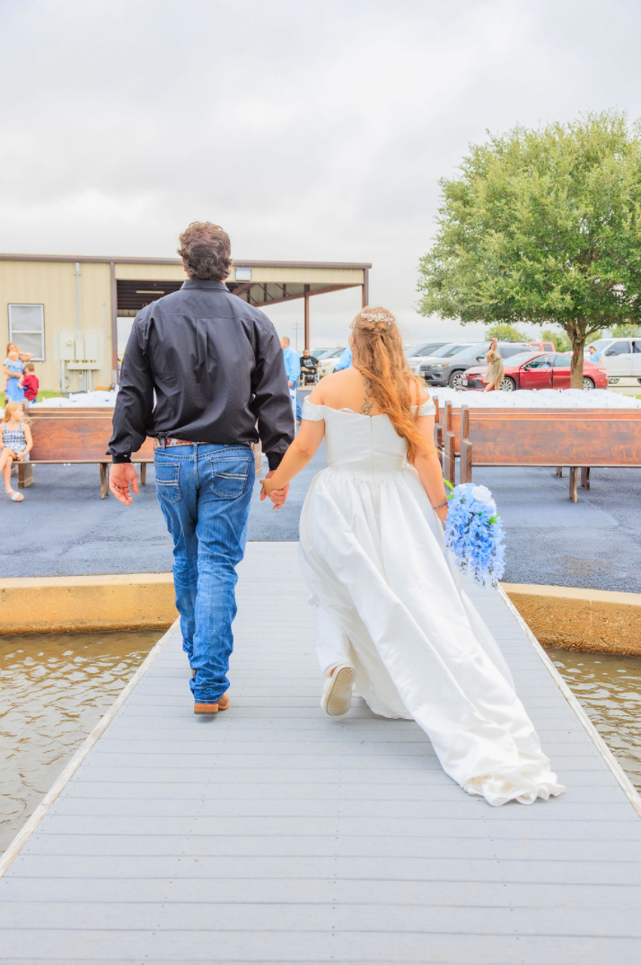 Jaelyn & Keelan's wedding at Reverie at Diamond D — the newlyweds walking hand in hand down the pavilion dock over the water