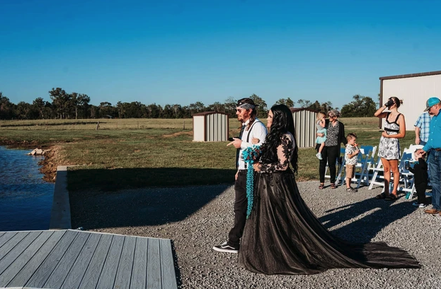 Couple standing beside the pond before the ceremony as guests gather on the gravel