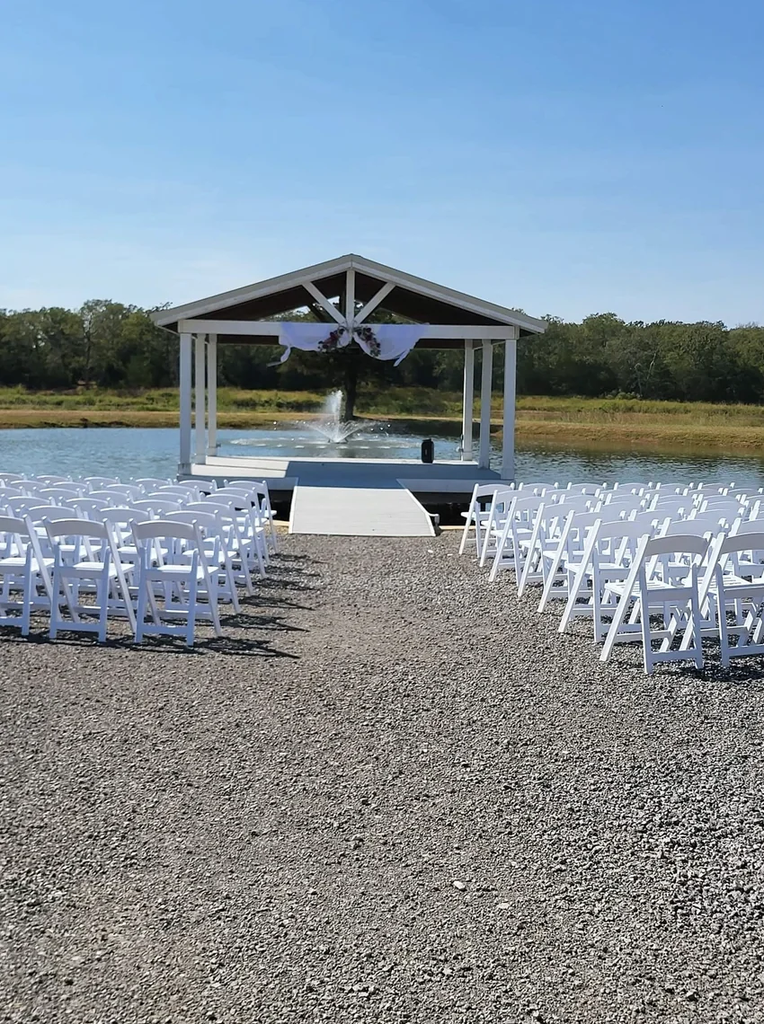 Rows of white folding chairs facing the lakeside pavilion and fountain before a wedding ceremony in Normangee, Texas