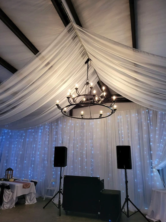 Wrought-iron chandelier and white ceiling draping above the twinkle-light backdrop in the barn