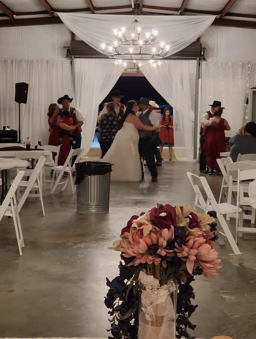 Wedding guests and couples dancing beneath an iron chandelier and white draping inside the Reverie reception hall