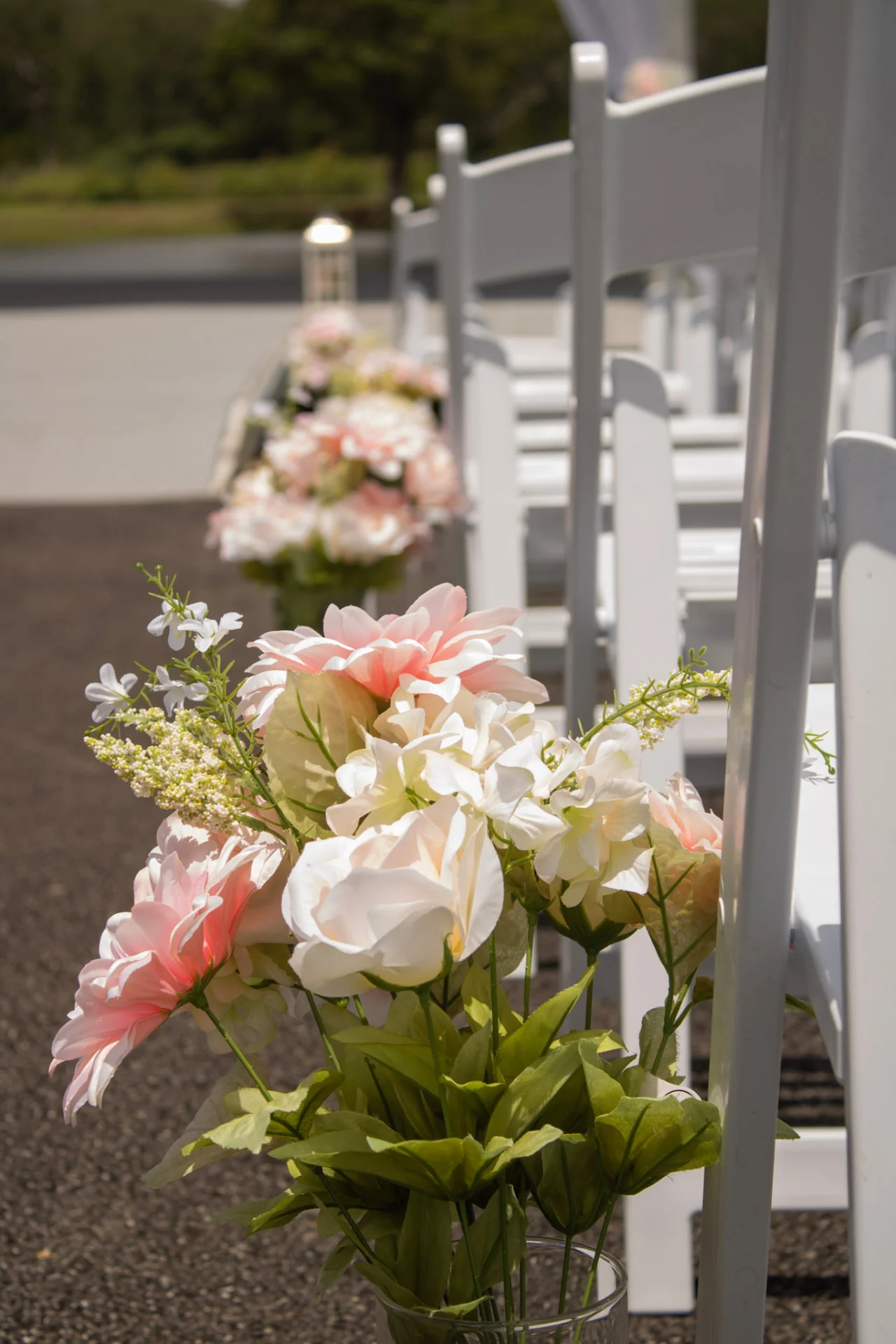Blush and ivory floral arrangements lining the ceremony aisle chairs outdoors