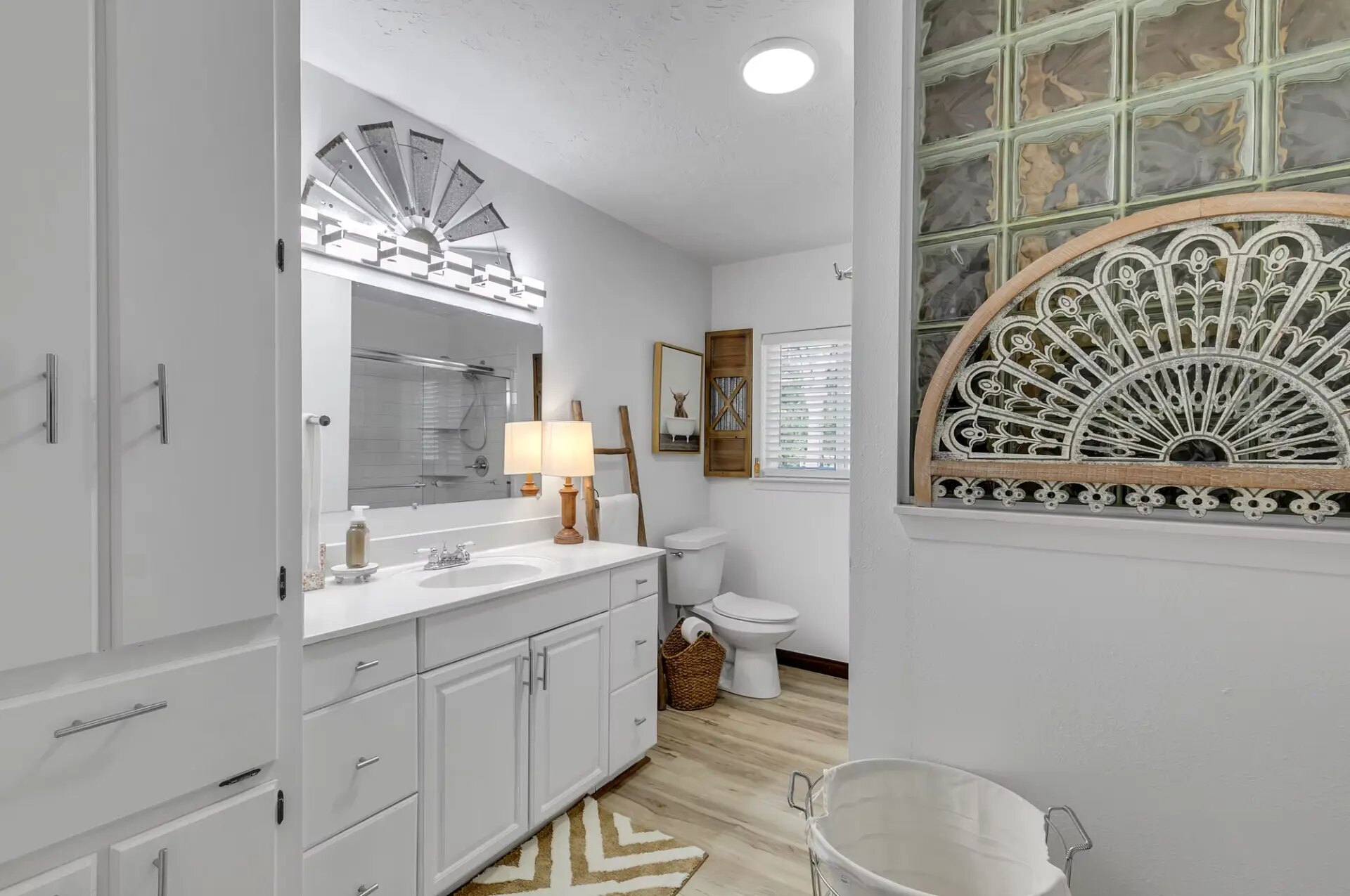 Farmhouse primary bathroom with double vanity, windmill light fixture and glass block window at Reverie at Diamond D