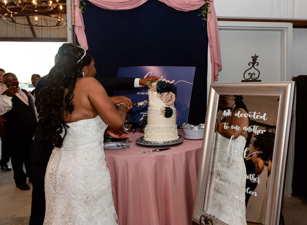 Bride and groom cutting their wedding cake beside a mirrored scripture sign