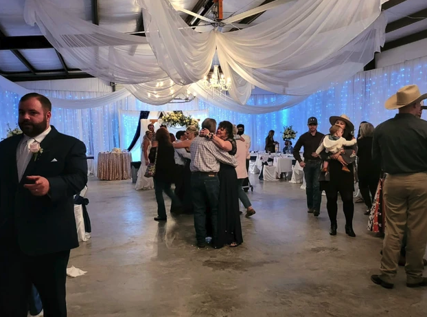 Guests dancing beneath white ceiling draping and blue twinkle-light curtains in the barn