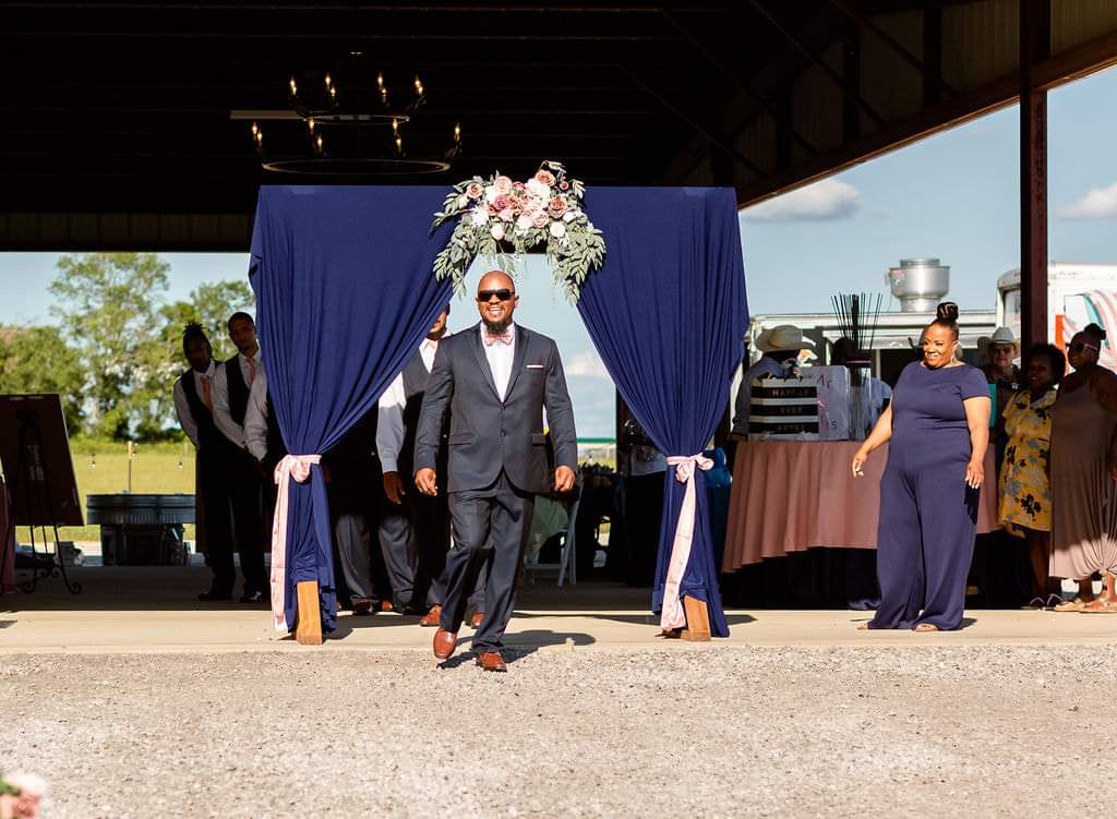Groom making his grand entrance through the navy and blush floral arch