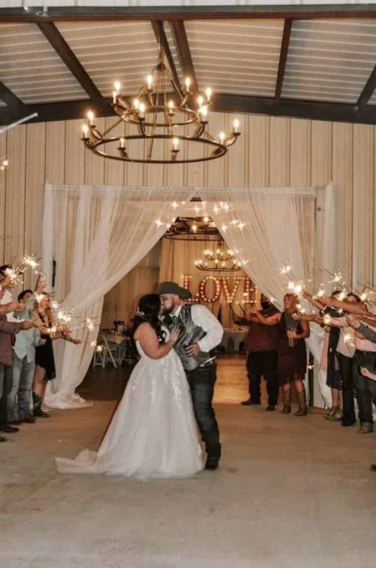 Cole and Emily kissing during their wedding send-off beneath chandeliers with a lighted LOVE marquee behind them