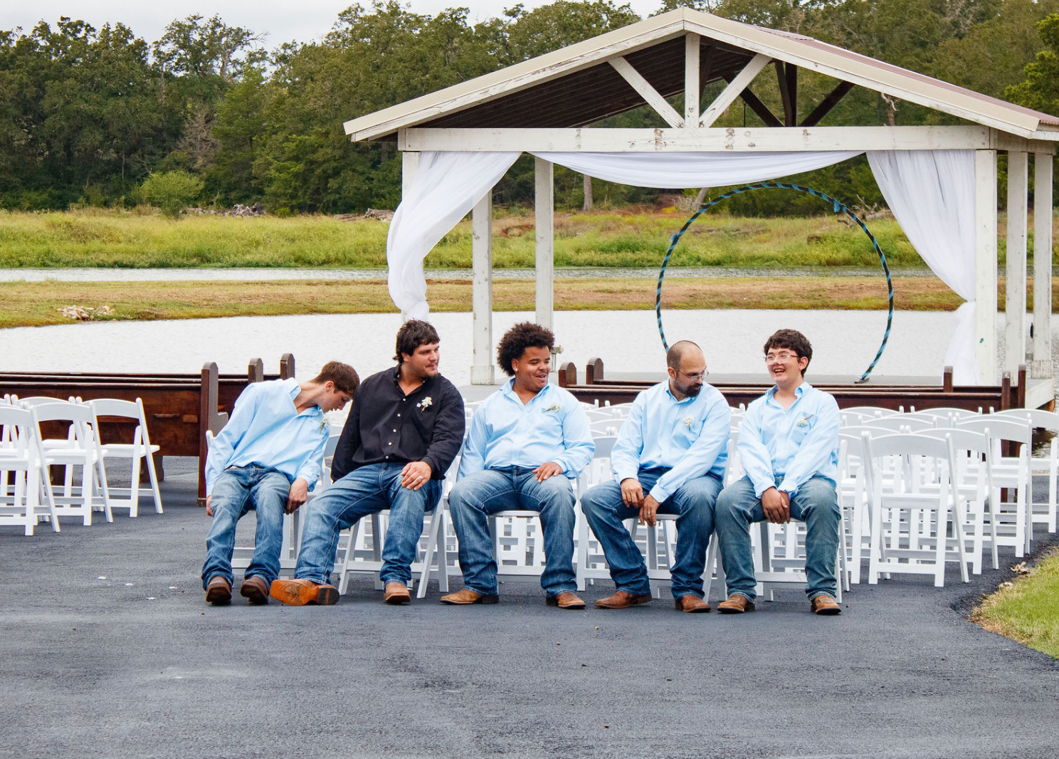 Jaelyn & Keelan's wedding at Reverie at Diamond D — the groom and groomsmen seated before the lakeside ceremony pavilion